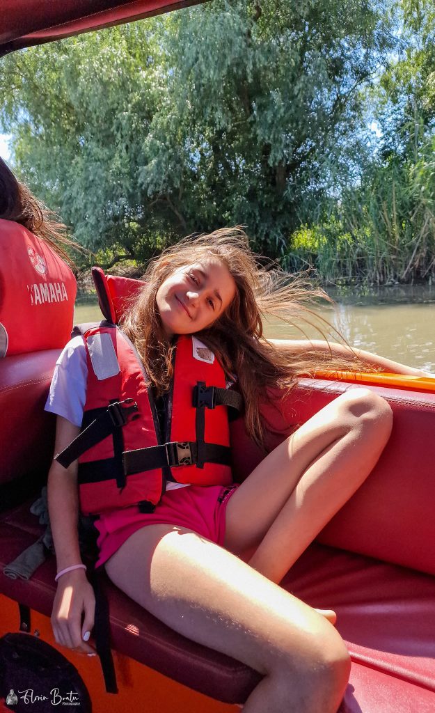 Excursii Delta Dunarii- O fată în vestă de salvare așezată în spatele unei bărci, bucurându-se de activitățile acvilele, asigurându-și în același timp siguranța.